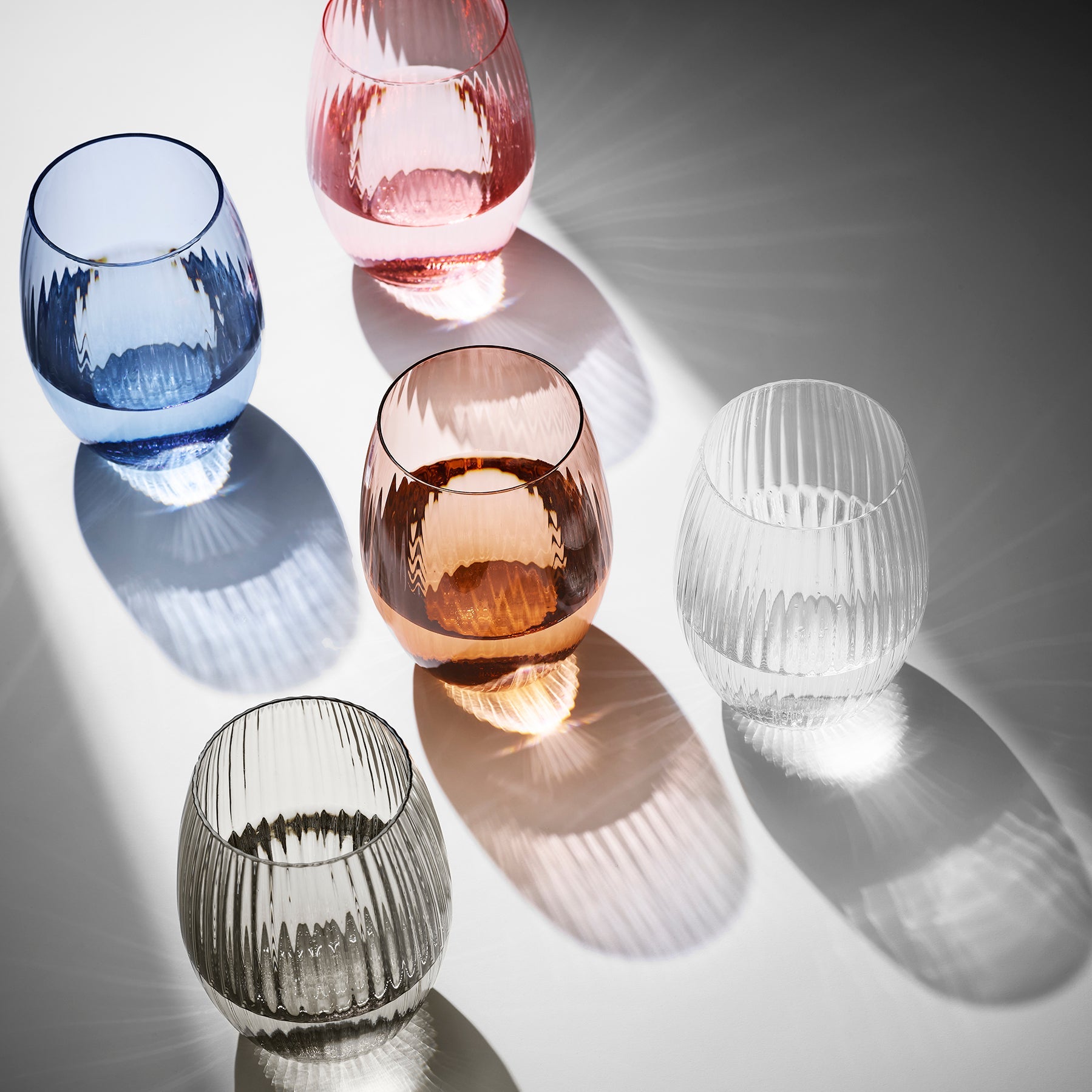 A set of colored wine glasses on a white surface.