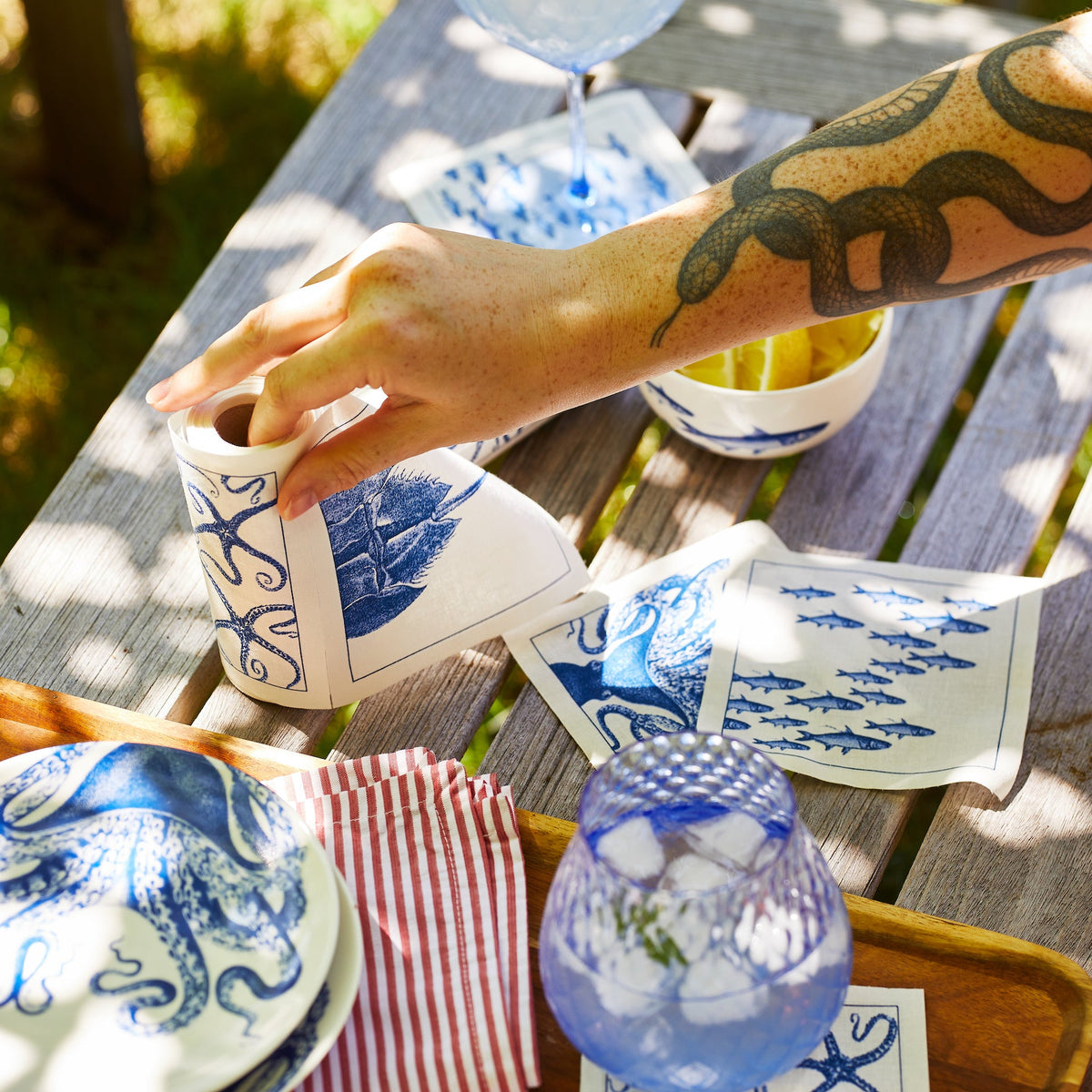 A person with tattoos hosting at a table with MY DRAP Coastal Cocktail Napkin Roll.