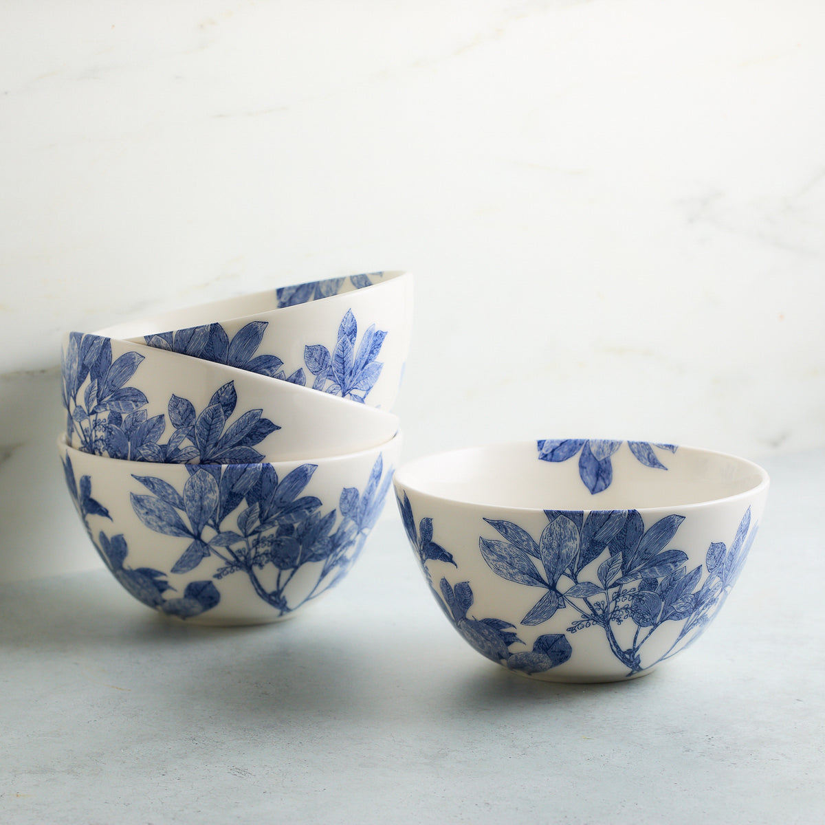 Four premium Arbor Cereal Bowls by Caskata with blue floral patterns stacked and arranged on a light gray surface against a white background.