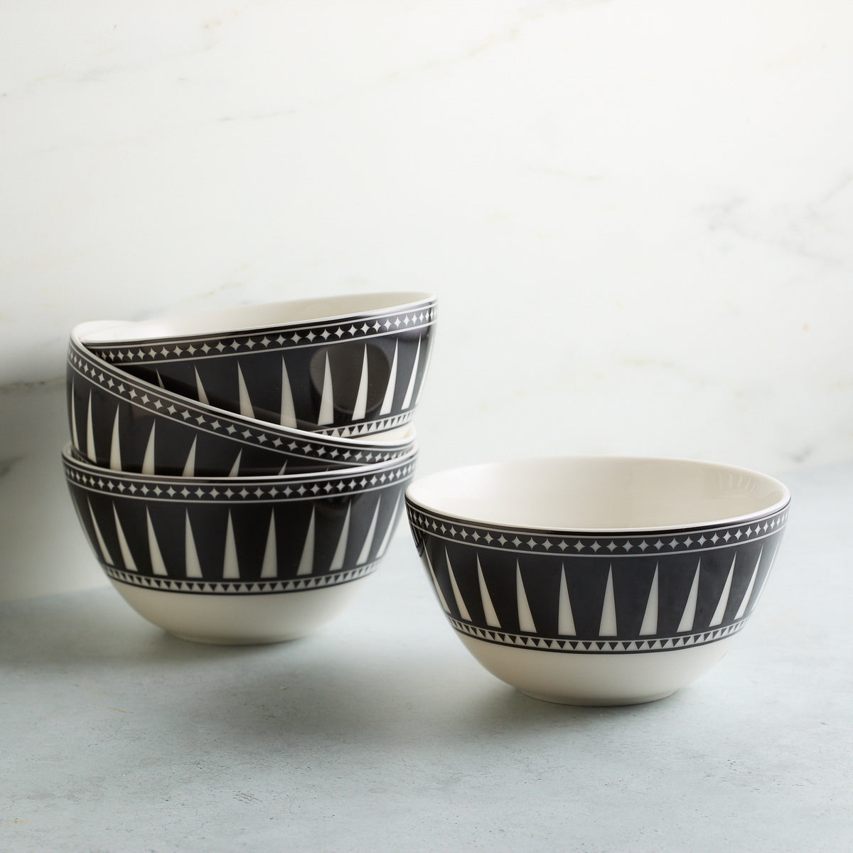 Four high-fired porcelain Marrakech Cereal Bowls by Caskata Artisanal Home with black and white geometric patterns are stacked on a light gray surface against a white background. These Marrakech-inspired bowls offer a touch of exotic elegance to your dining experience.