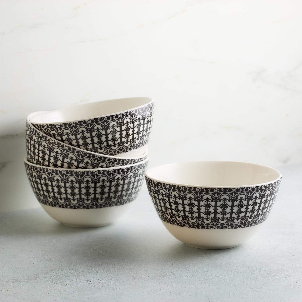 Four Casablanca Cereal Bowls by Caskata Artisanal Home with intricate black and white patterns stacked against a white marble background.