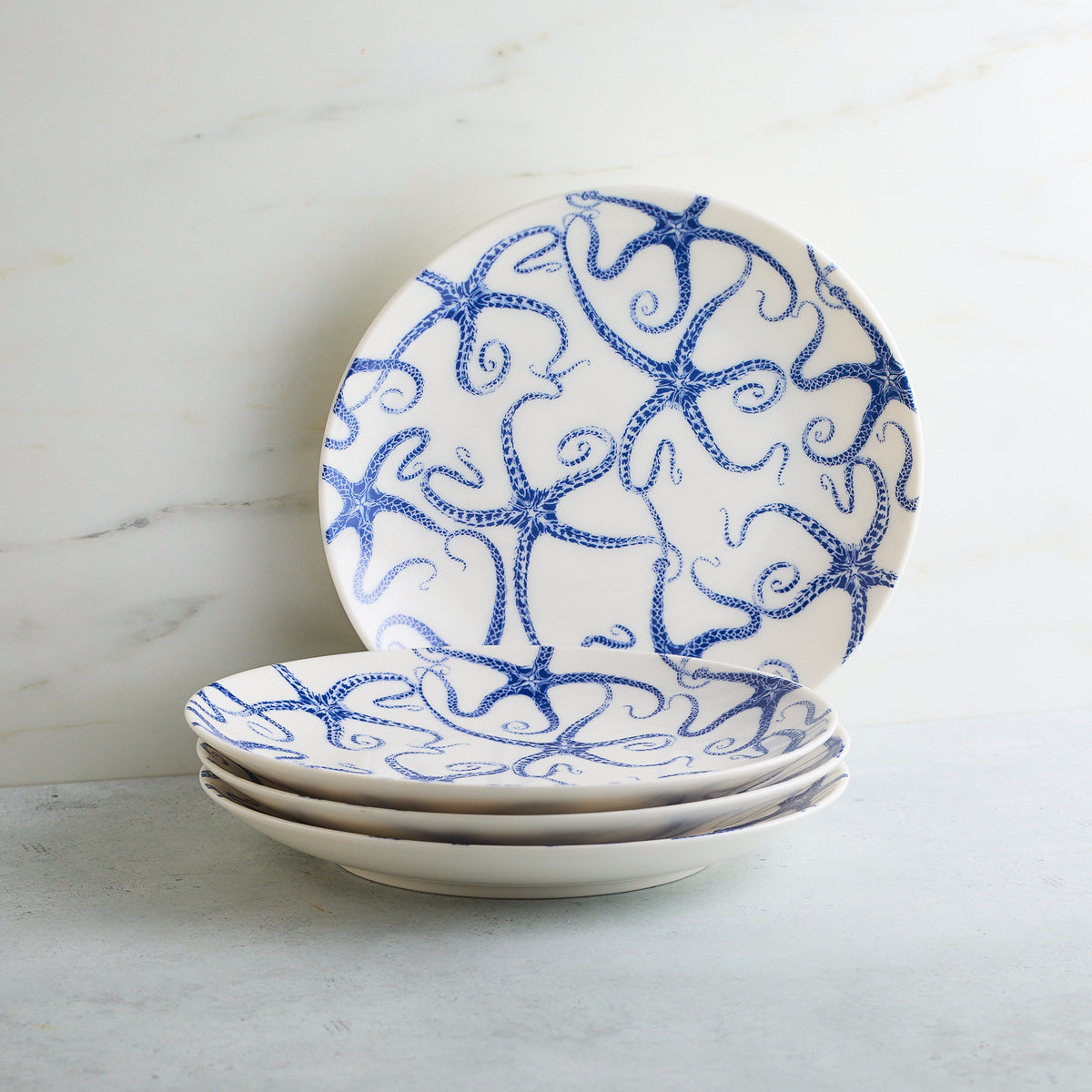 A stack of Caskata Artisanal Home Starfish Coupe Salad Plates adorned with blue starfish designs against a light background.