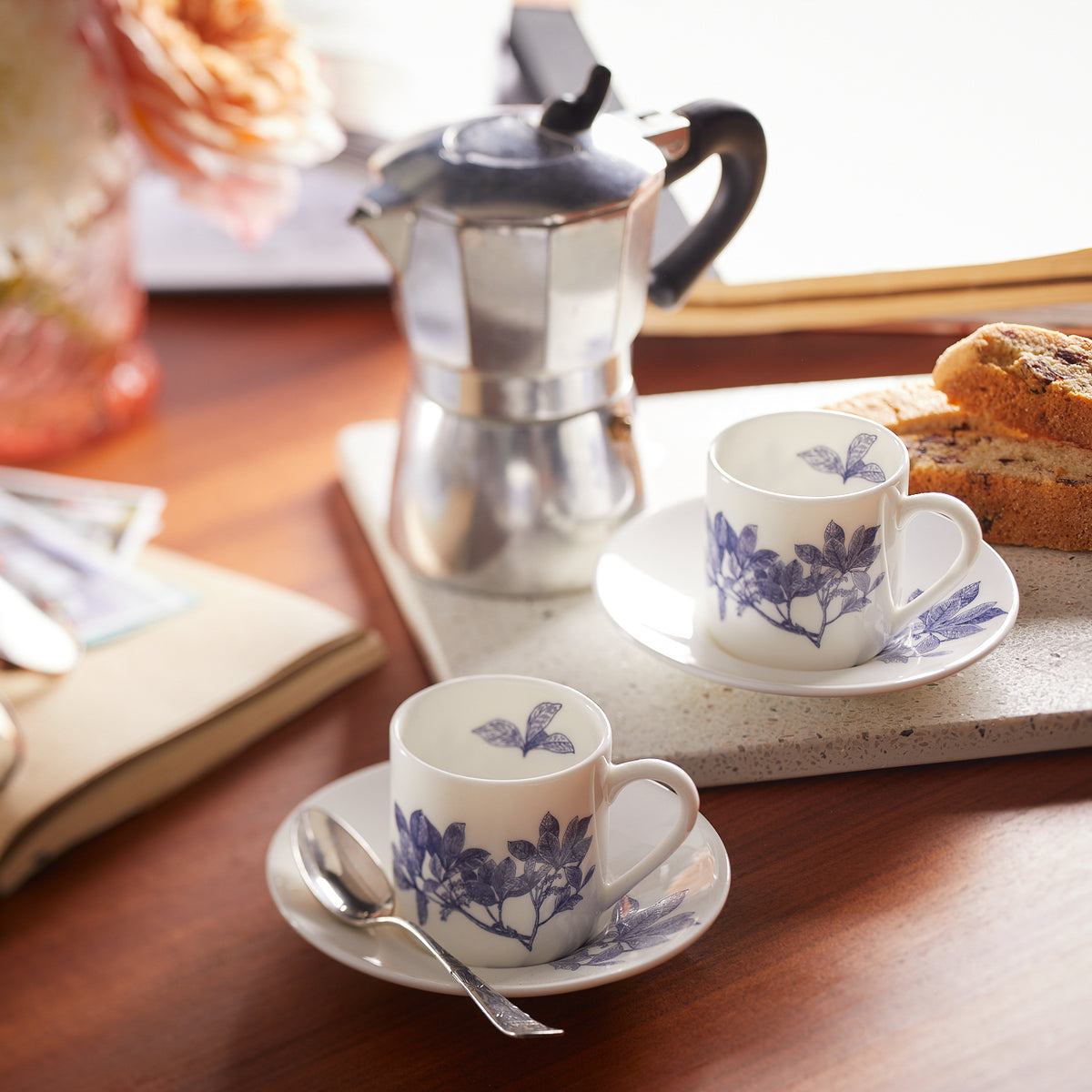 Two Arbor Espresso Cups &amp; Saucers, Set of 2, by Caskata with blue floral designs, part of a blue and white dinnerware set, sit on saucers next to a silver coffee maker and sliced bread on a tray on a wooden table.
