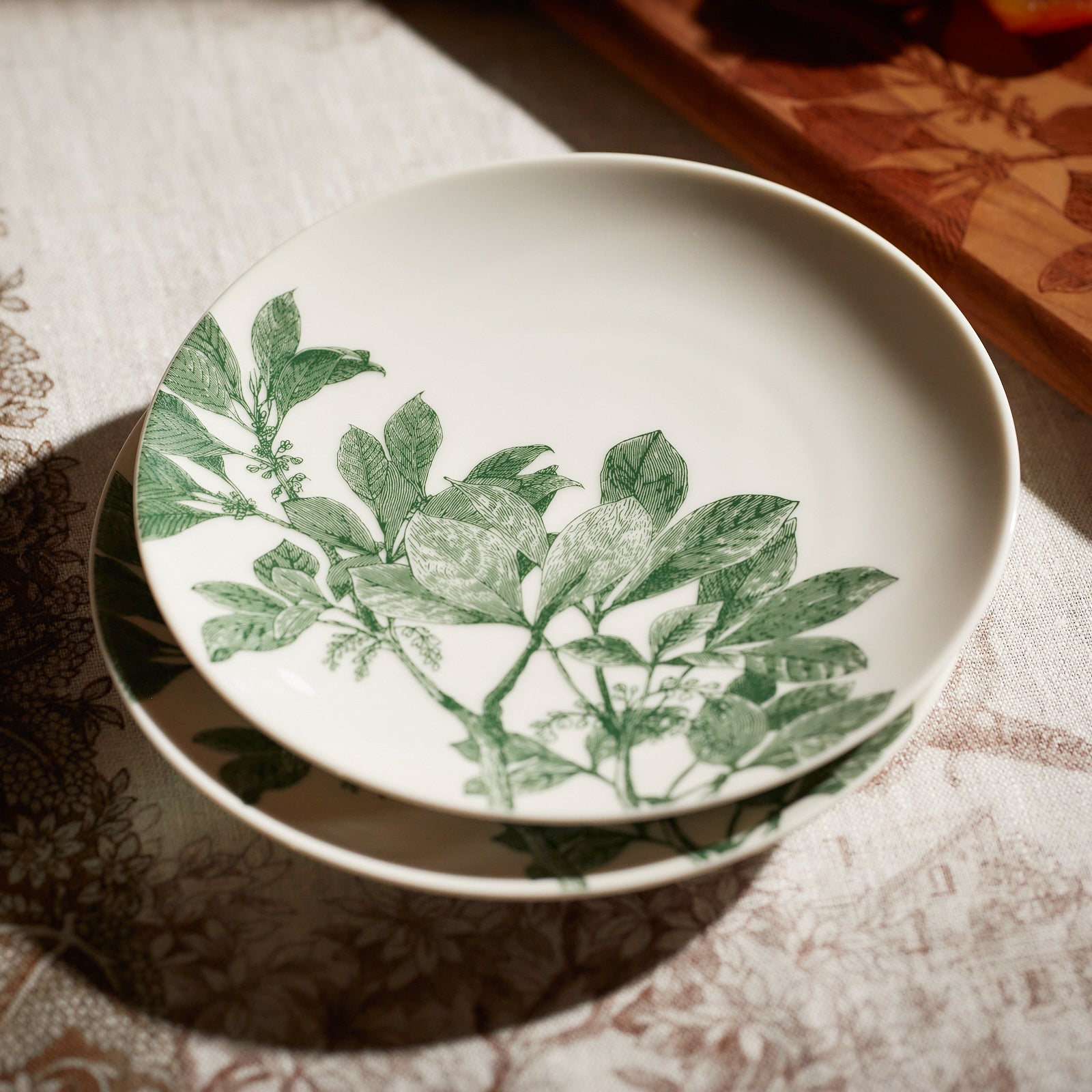 Four Caskata Arbor Green Small Plates with green leaf patterns are arranged in a semi-overlapping manner, creating a delightful botanical dinnerware display.