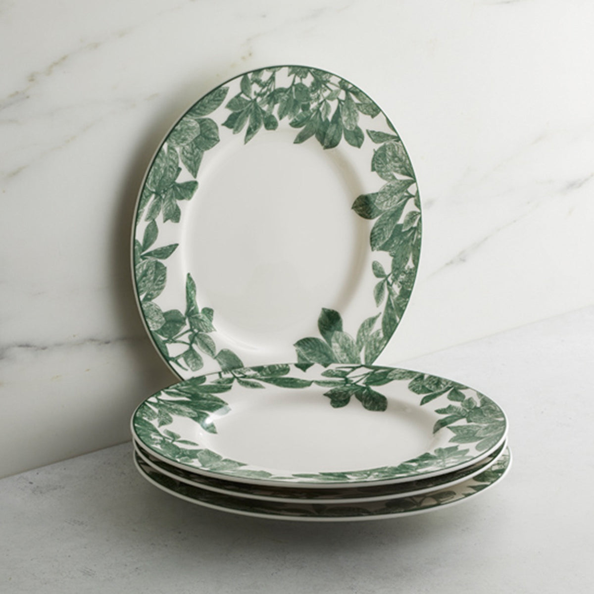Three Caskata Arbor Green Rimmed Salad Plates are stacked neatly on a light-colored surface against a marble background.