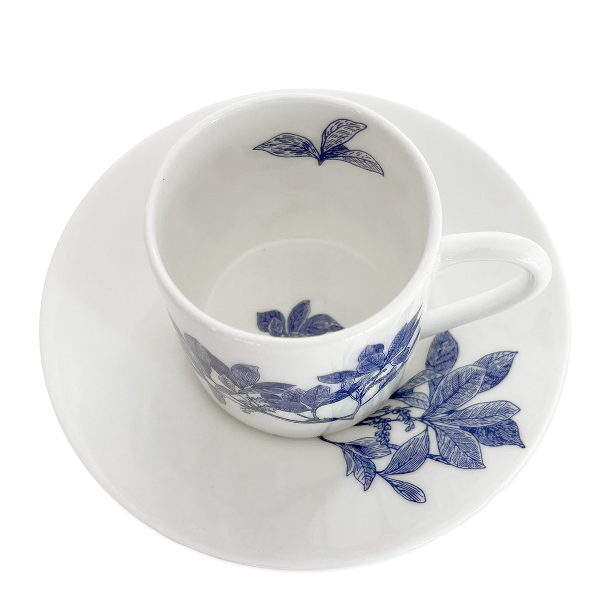 A set of Arbor Espresso Cups &amp; Saucers, Set of 2 by Caskata, featuring a white ceramic design with blue floral patterns, perfect for your Blue and White Dinnerware collection. The espresso cup, made of elegant Bone China, is placed gracefully on the matching saucer.