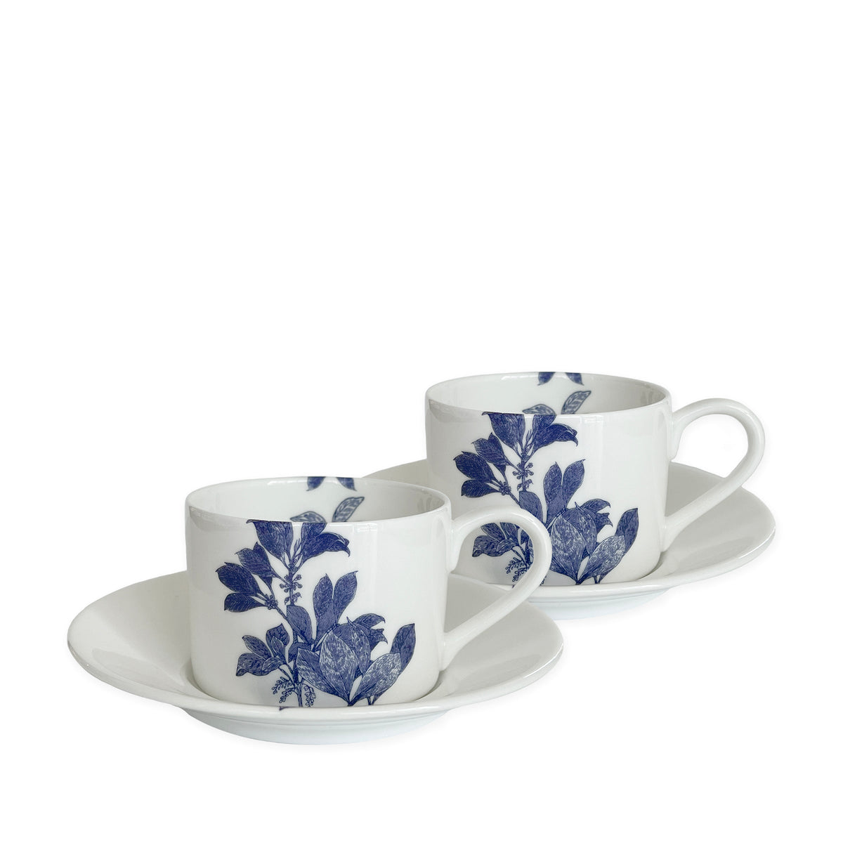 Two white bone china cups with matching saucers, decorated with blue floral patterns, are placed side by side against a white background. This elegant blue and white dinnerware, the Arbor Cups &amp; Saucers, Set of 2 from Caskata Artisanal Home, is both dishwasher and microwave safe.