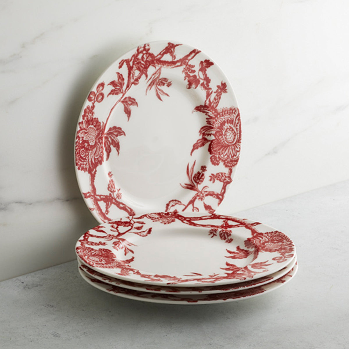 A stack of three Caskata Artisanal Home Arcadia Crimson Rimmed Salad Plates, reminiscent of premium porcelain dinnerware, set against a marble background.