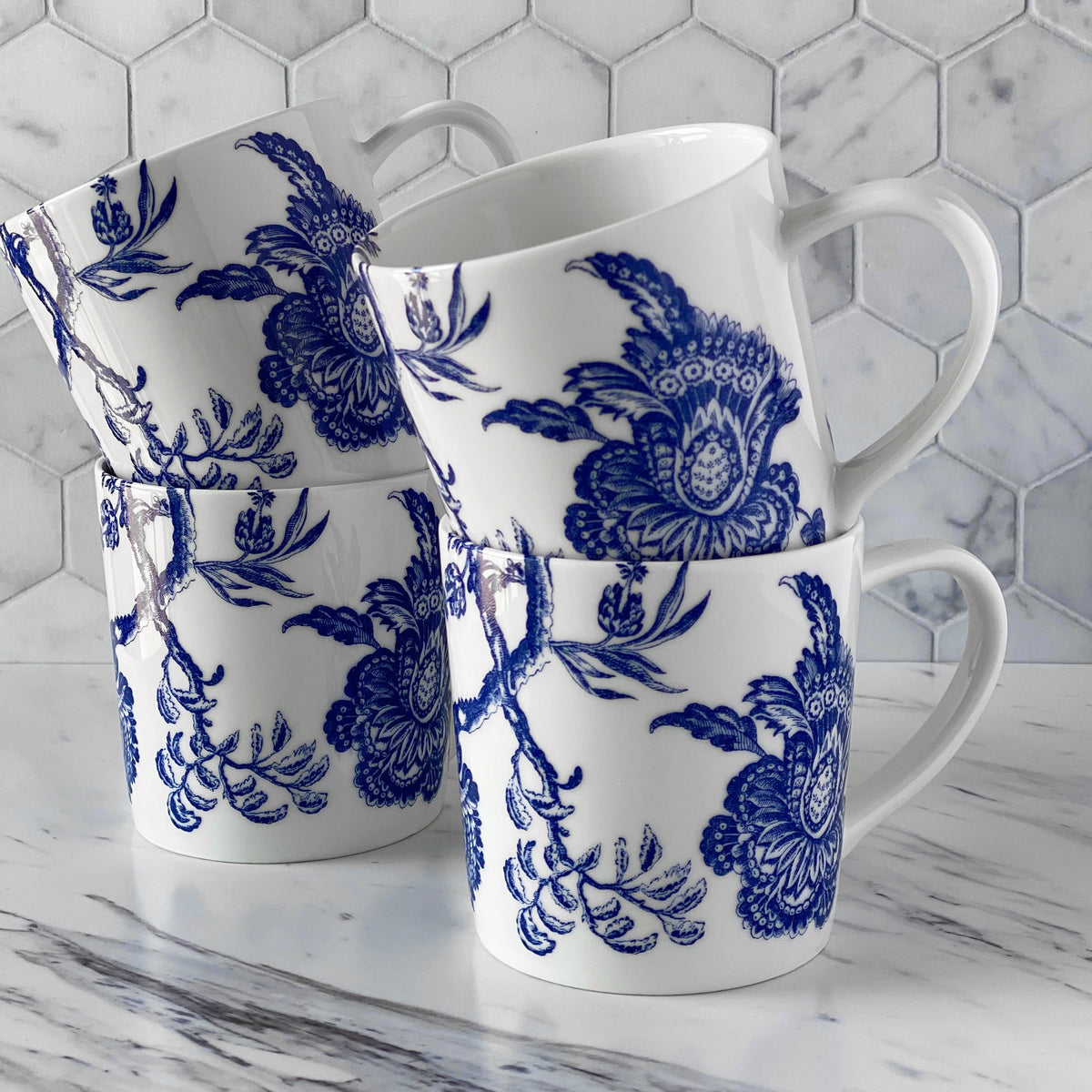 The set of 4 blue and white porcelain Arcadia Mugs from Caskata displayed in a bright marble kitchen.