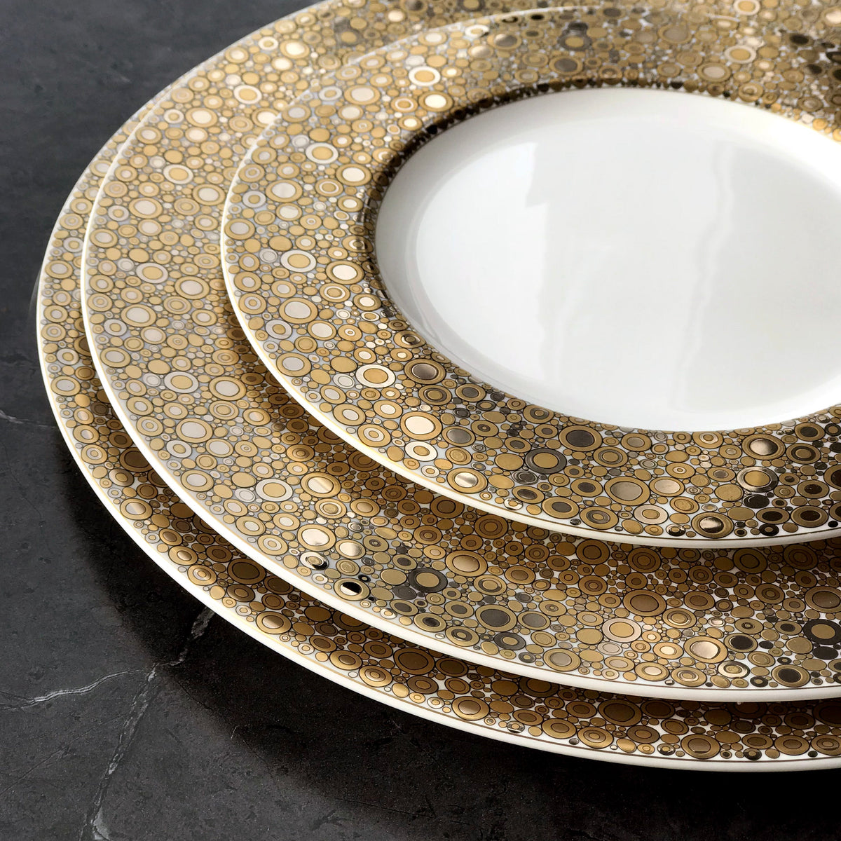 A set of Caskata Artisanal Home Ellington Shimmer Gold &amp; Platinum Charger Plates on a marble table.