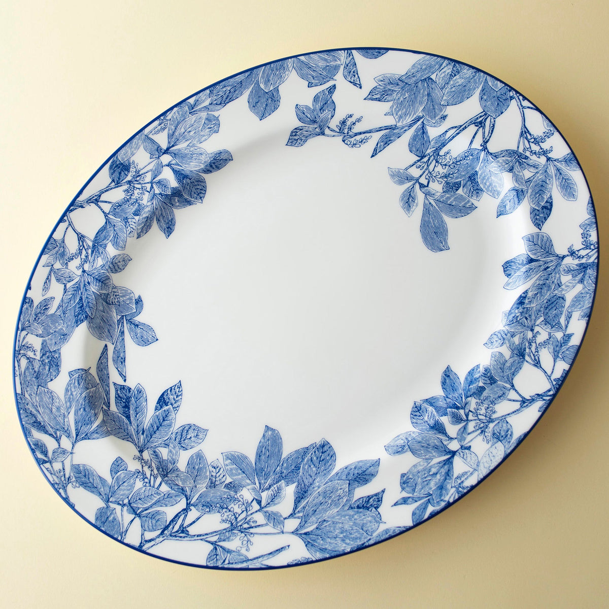 An oval ceramic plate with a blue floral pattern along the rim, set against a plain background, this Arbor Oval Rimmed Platter by Caskata Artisanal Home exudes high style and elegance.