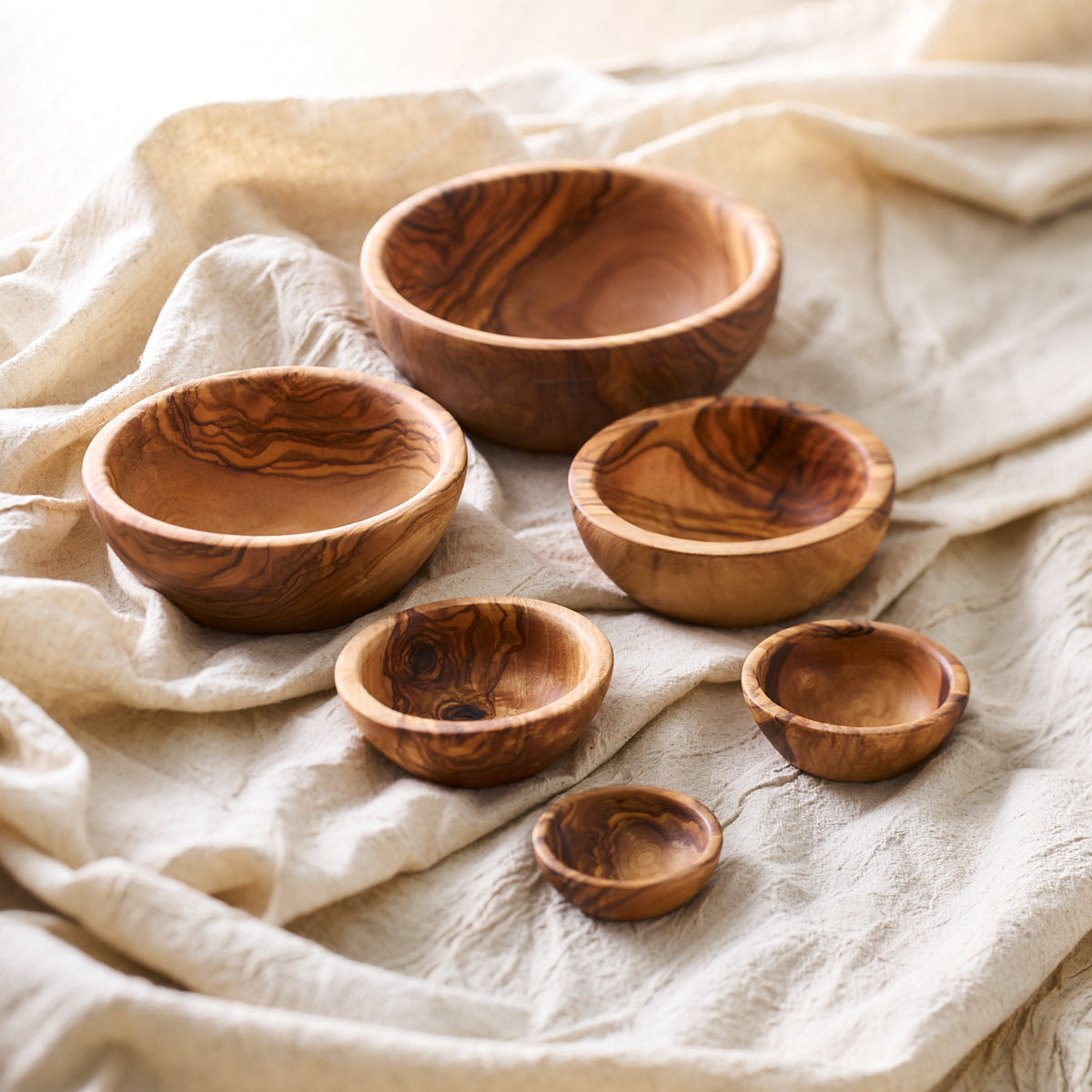 A set of Be Home Olive Wood Nesting Bowls, Set of 6 on a white cloth.