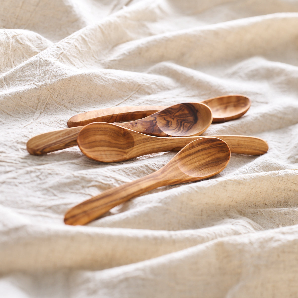 Three Be Home Olive Wood Small Spoons, Set of 4 on a white linen.