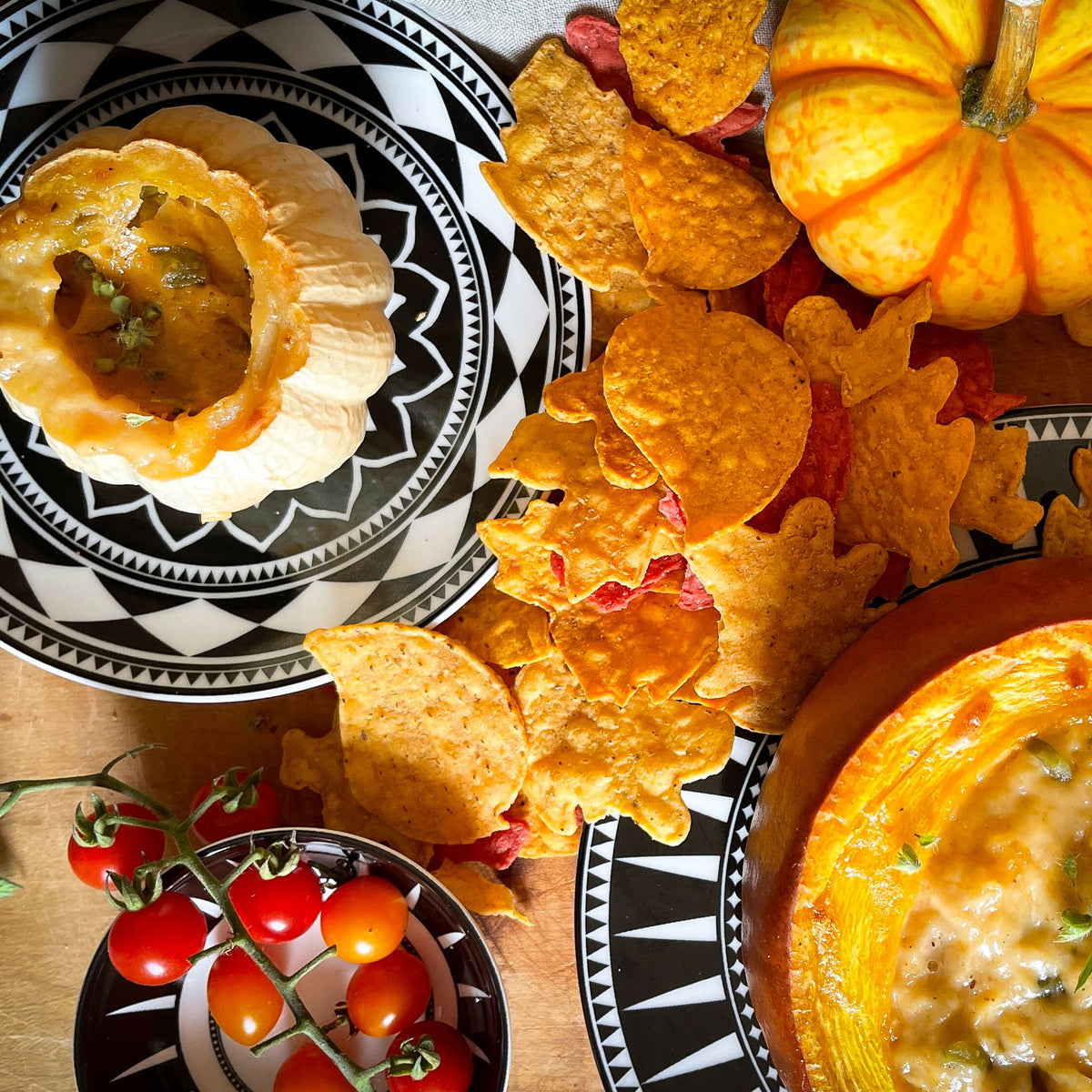 Festive fall-themed table with pumpkin-shaped bowls containing dip, surrounded by leaf-shaped chips, tomatoes, and a pumpkin for decoration, featuring Fez Small Plates by Caskata Artisanal Home that complement the autumn ambiance.