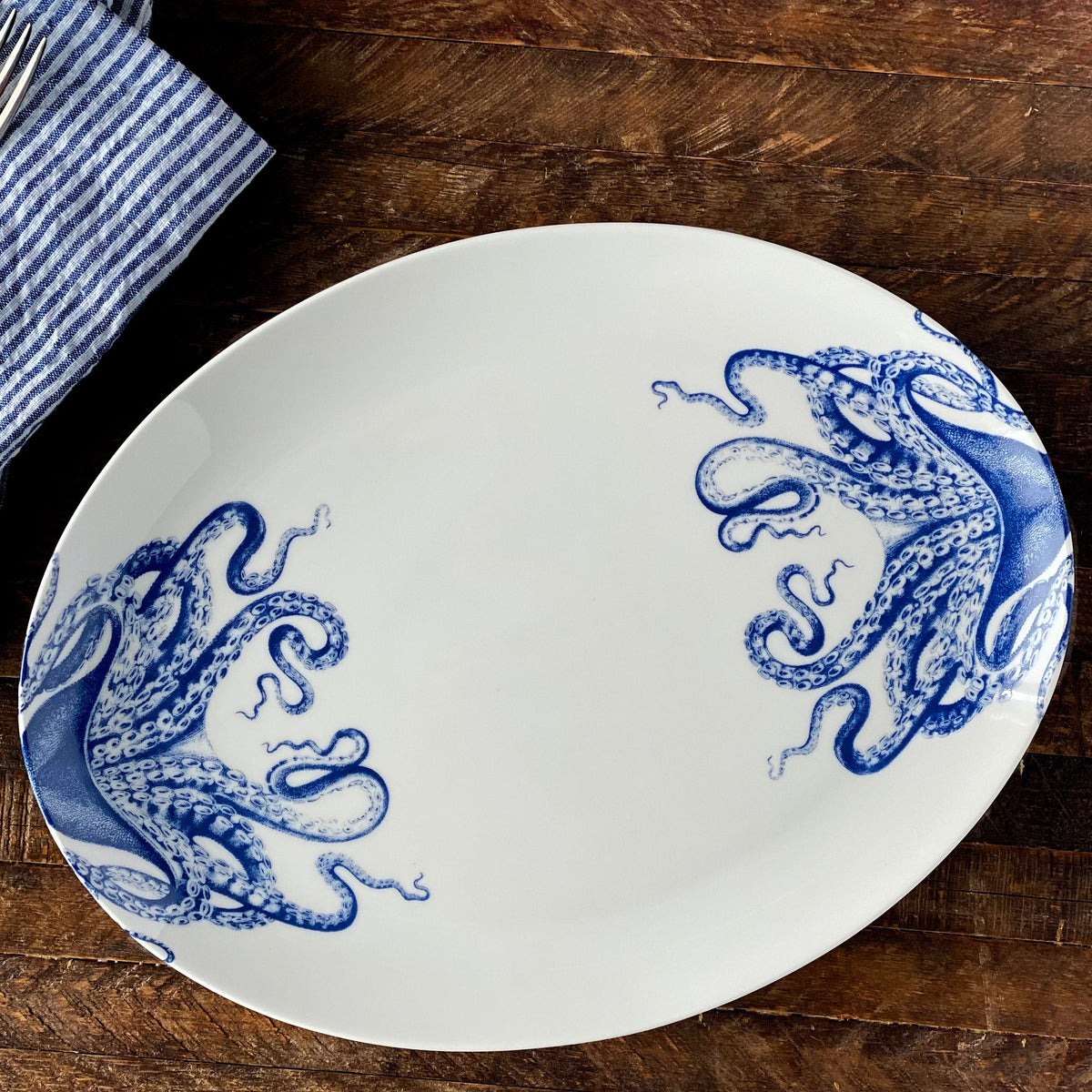 A blue on white porcelain Lucy Coupe Platter by Caskata on a rustic wooden tabletop.