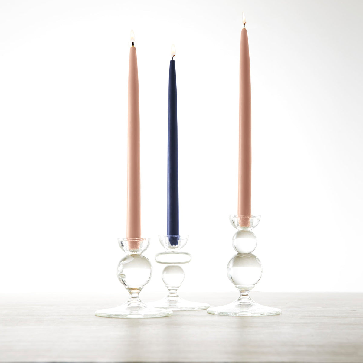 Three 12&quot; Petal Pink Taper Candles - Set of 2, by Floral Society, are sitting on a table next to each other.