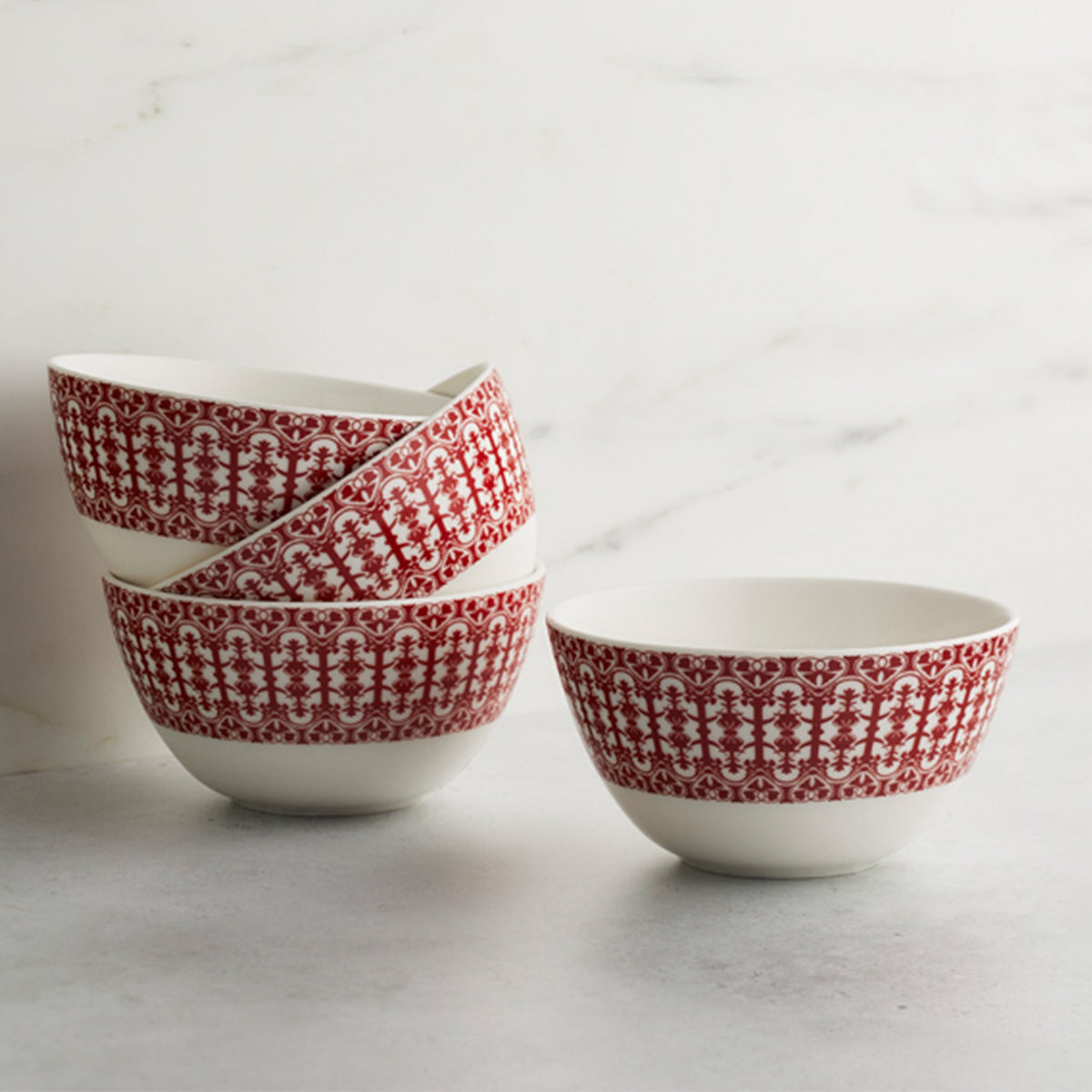 Four Caskata Casablanca Crimson Cereal Bowls are stacked on a marble surface against a white background.