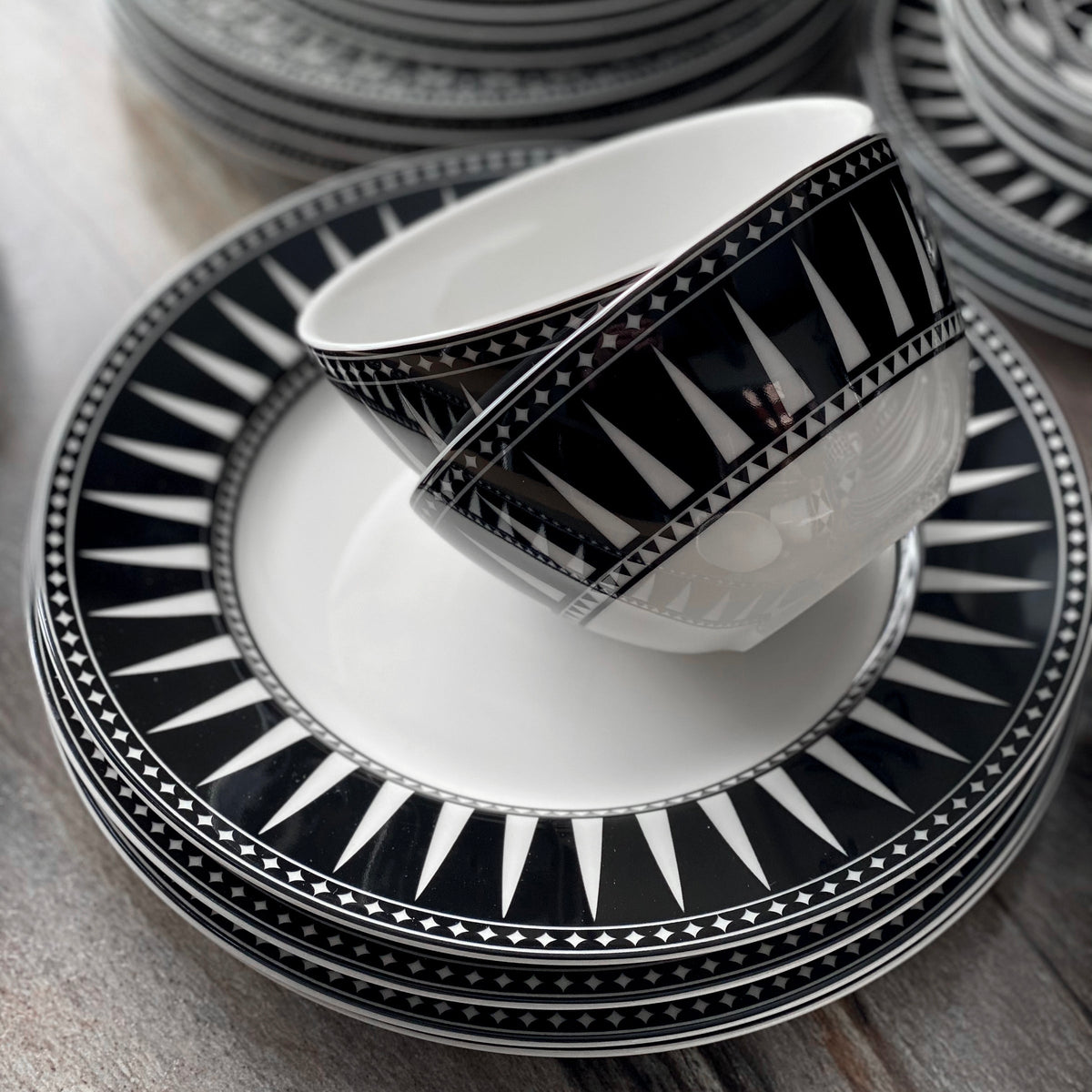A Caskata Artisanal Home dinnerware collection featuring graphic patterns of Moroccan-inspired design, including the Geometrics Collection 60 Pc. Set plates and cups on a table.