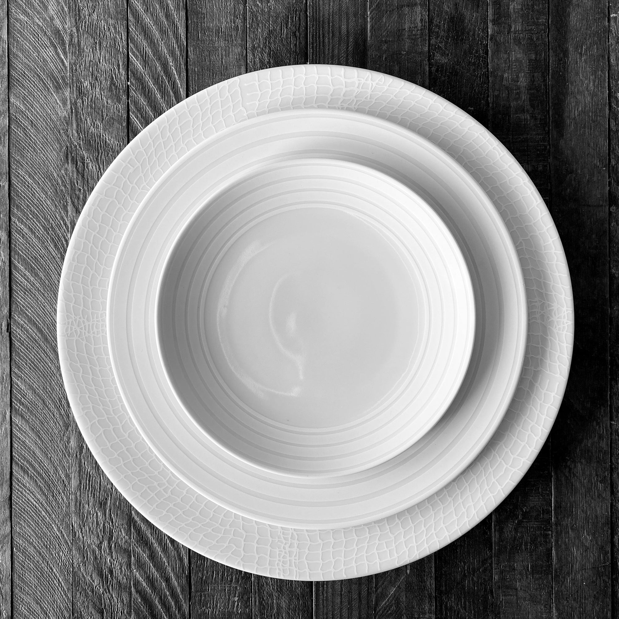 Four white, round plates with simple, concentric circle designs on the edges in the elegant **Cambridge Stripe Small Plates** pattern are arranged in a staggered layout against a plain white background. **Caskata Artisanal Home**