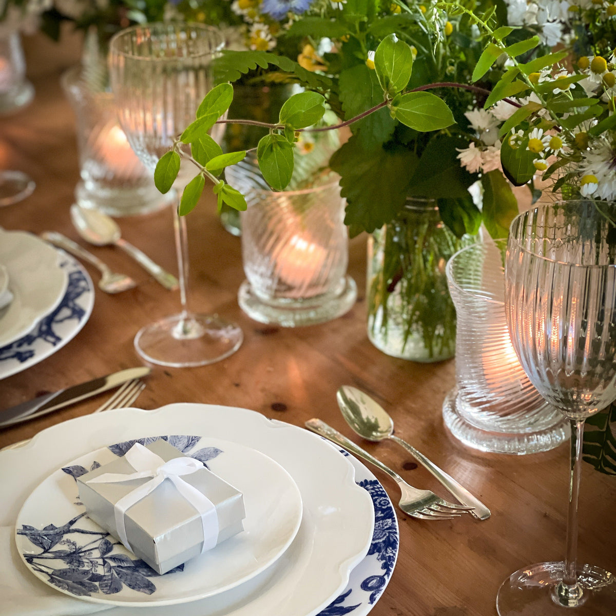 Caskata&#39;s Quinn Clear Votives are centerstage in this example of a spring tablescape that features Quinn Clear White Wine glasses, Blue Arbor Canapes, Grace Buffet Plates, Arcadia Dinner Plates and leafy green bouquets.
