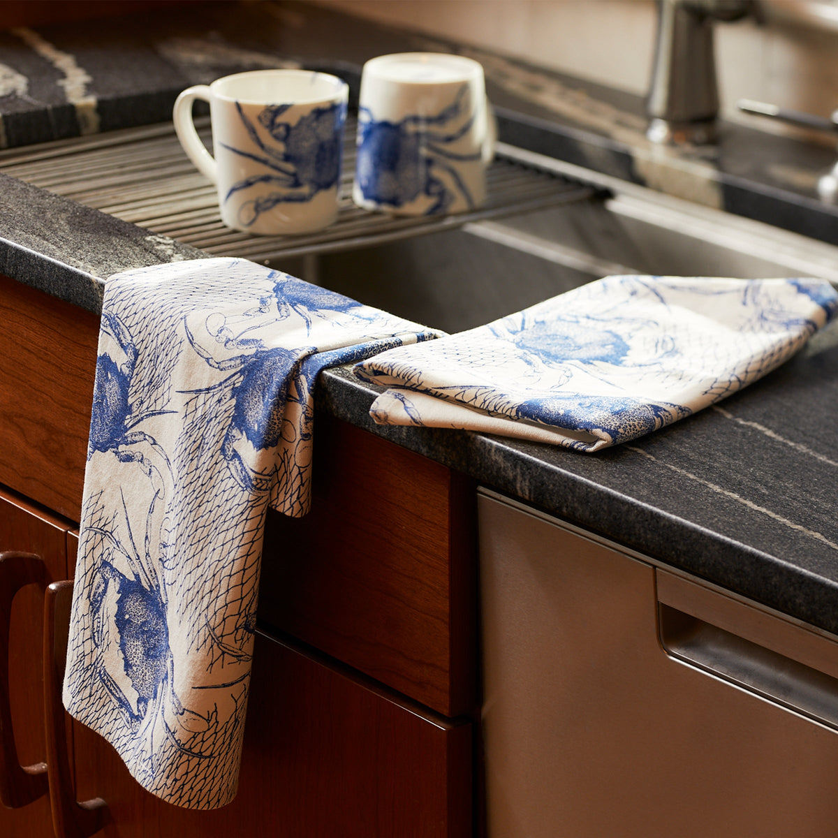 A kitchen sink with a Crabs &amp; Nets Kitchen Towels Set/2 by Caskata on it, adding a touch of seafaring whimsy.