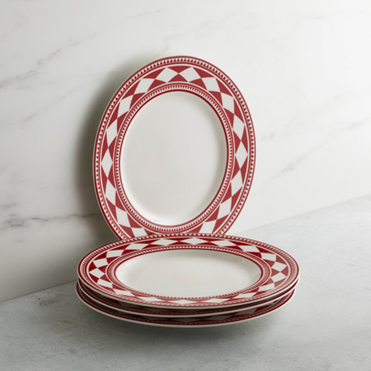A stack of four high-fired porcelain Caskata Artisanal Home Fez Crimson Rimmed Salad Plates, leaning against a white marble background.