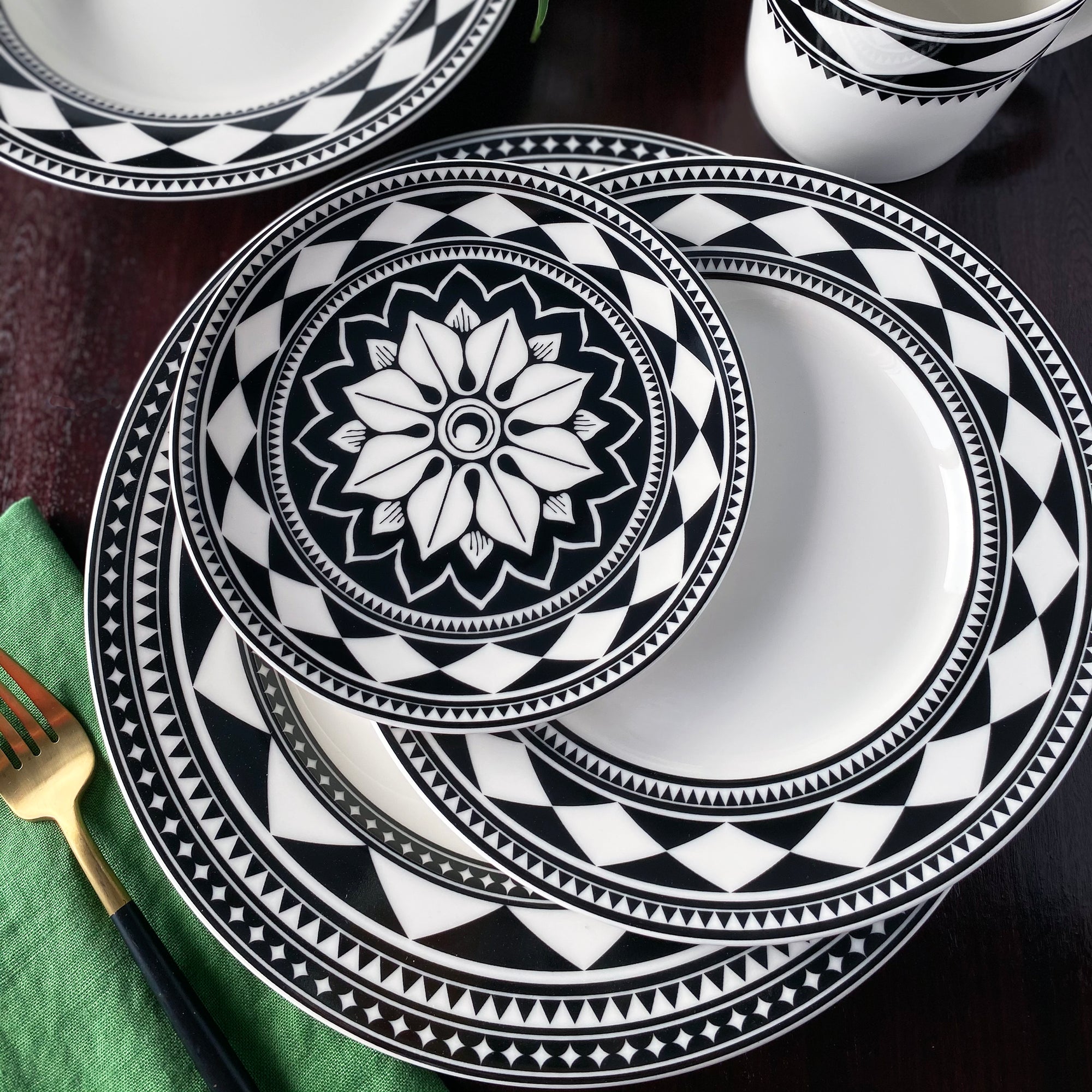 A Fez Rimmed Dinner Plate by Caskata Artisanal Home, a white plate with a wide rim, showcasing a black and white geometric pattern reminiscent of Moroccan designs.