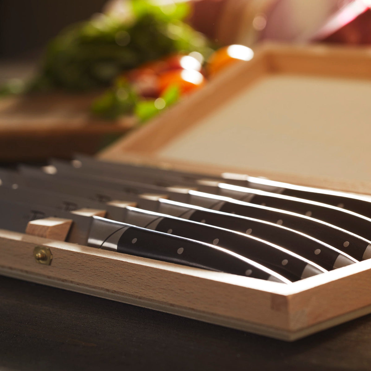 A Goyon-Chazeau Black Paperstone Steak Knives Boxed Set/6 in a wooden box on a table.