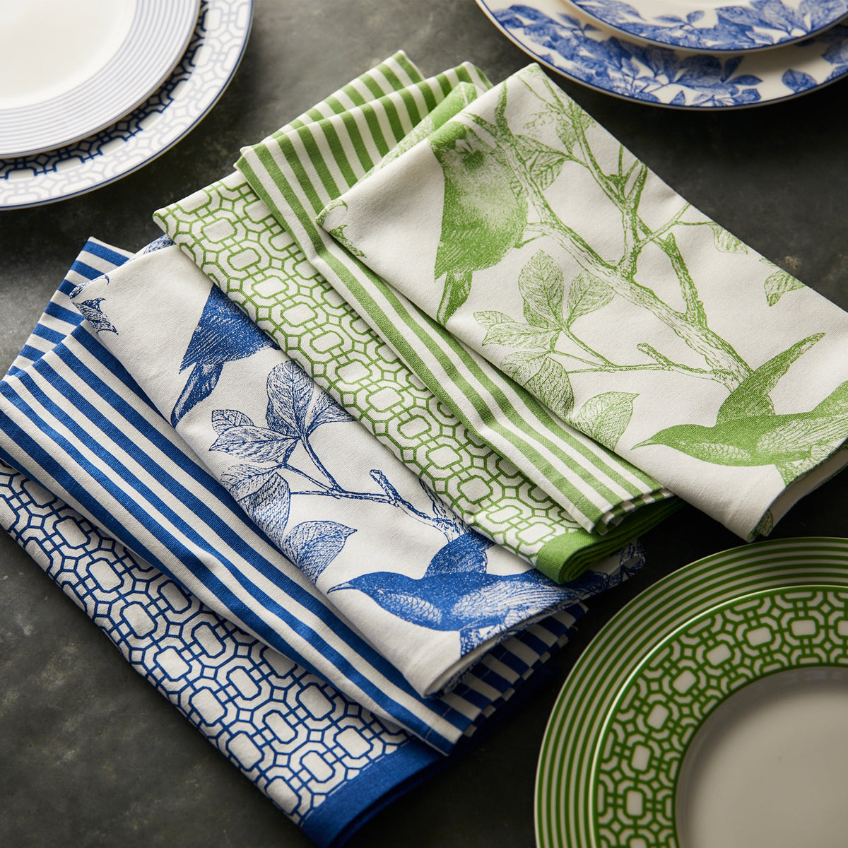 A set of Caskata Newport Garden Gate Dinner Napkins in Green Set/4 in blue and white on a table.