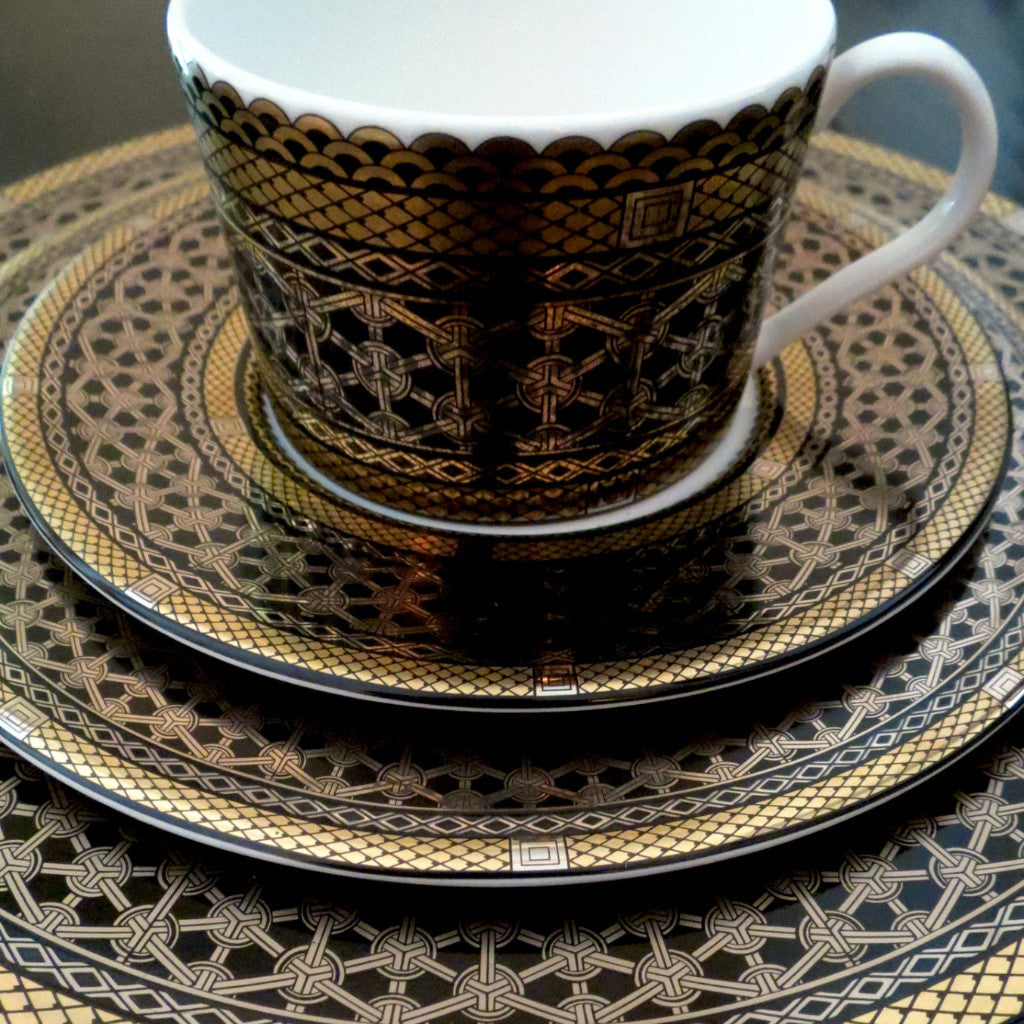 A black and gold Hawthorne Onyx Gold &amp; Platinum Bread &amp; Butter Plate by Caskata Artisanal Home on a table, perfect for luxurious tea or coffee moments.