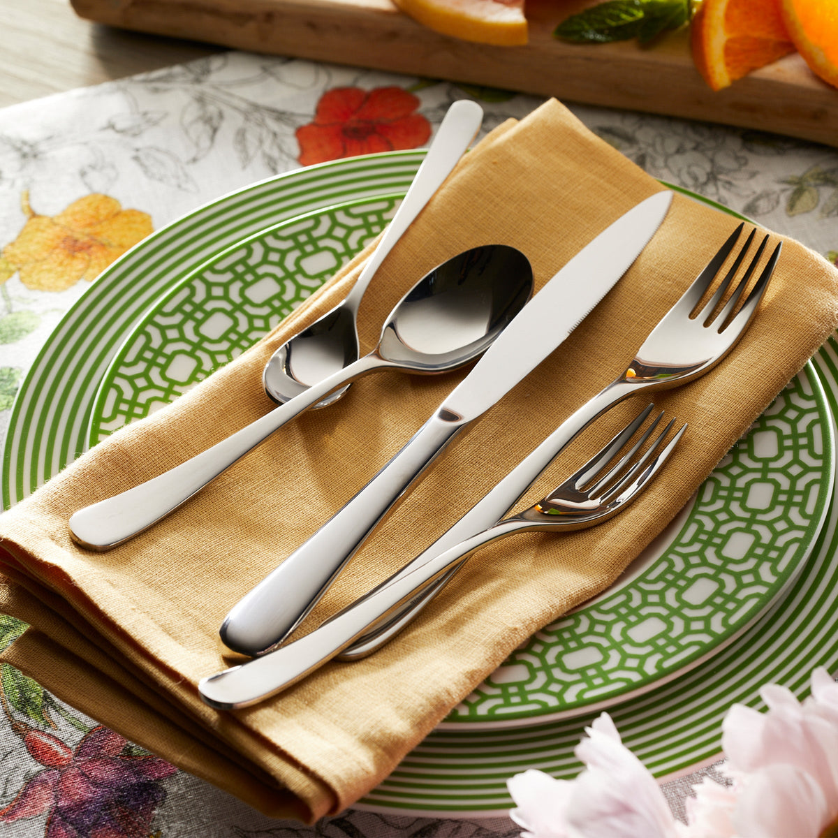 A La Mer 5-Piece Flatware Setting with a polished finish on a green plate in an elegant Degrenne setting.