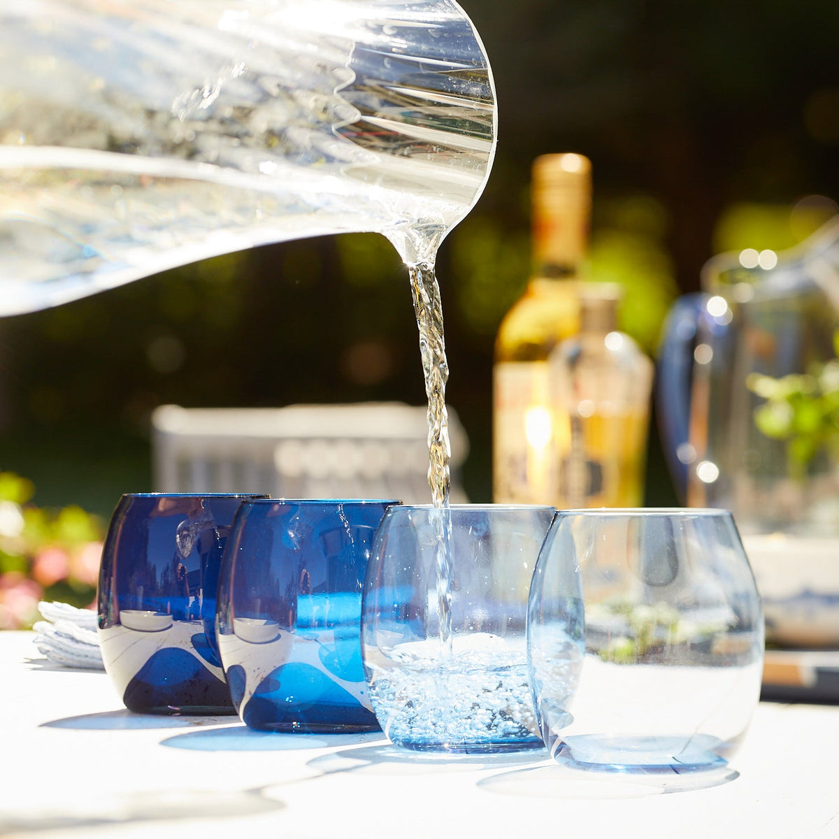 A person pouring water into Les Nuages Blue Ombré Glasses Set of 4 tumblers made by Caskata.