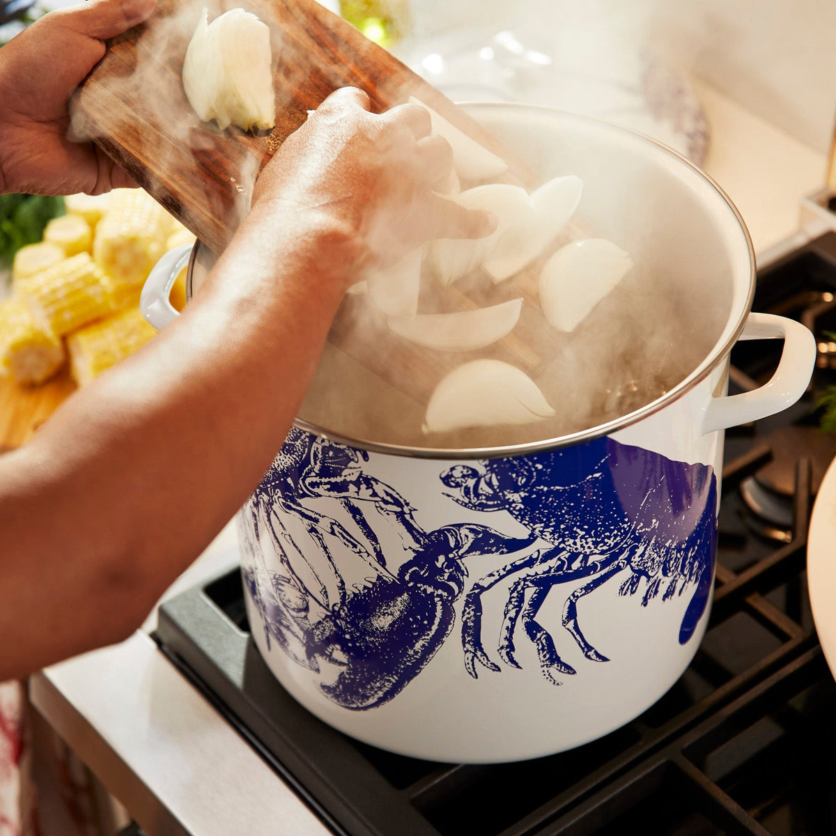 A person is preparing lobster in a Caskata X Cuisinart Limited Edition Lobster 16 Qt. Enamel on Steel Stockpot on the stove.