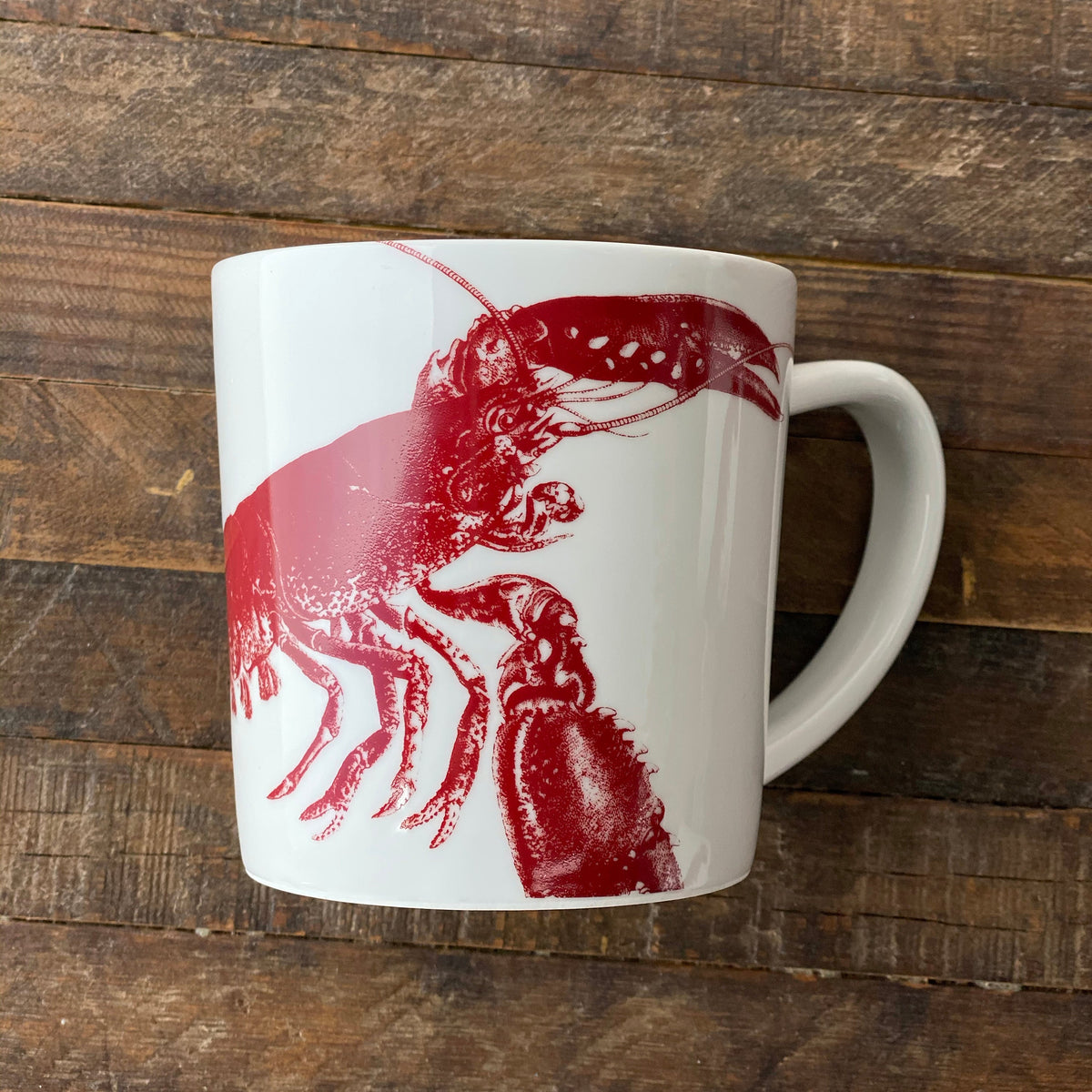Lobster Red Mug by Caskata Artisanal Home, crafted from high-fired porcelain, featuring a striking red lobster design and placed on a wooden surface, evoking a charming seaside style.