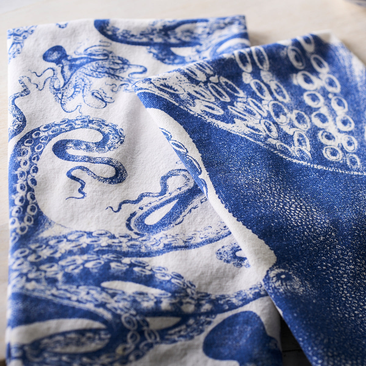 Two white cotton tea towels featuring intricate blue designs of octopus tentacles and sea creatures, laid flat on a surface. These kitchen companions add a touch of marine elegance to any culinary space. Introducing the Lucy Kitchen Towels, Set of 2 by Caskata.