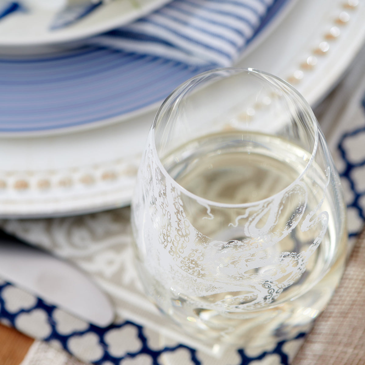 A Lucy Stemless Wine Glass from Caskata Artisanal Home sits elegantly on a table setting.