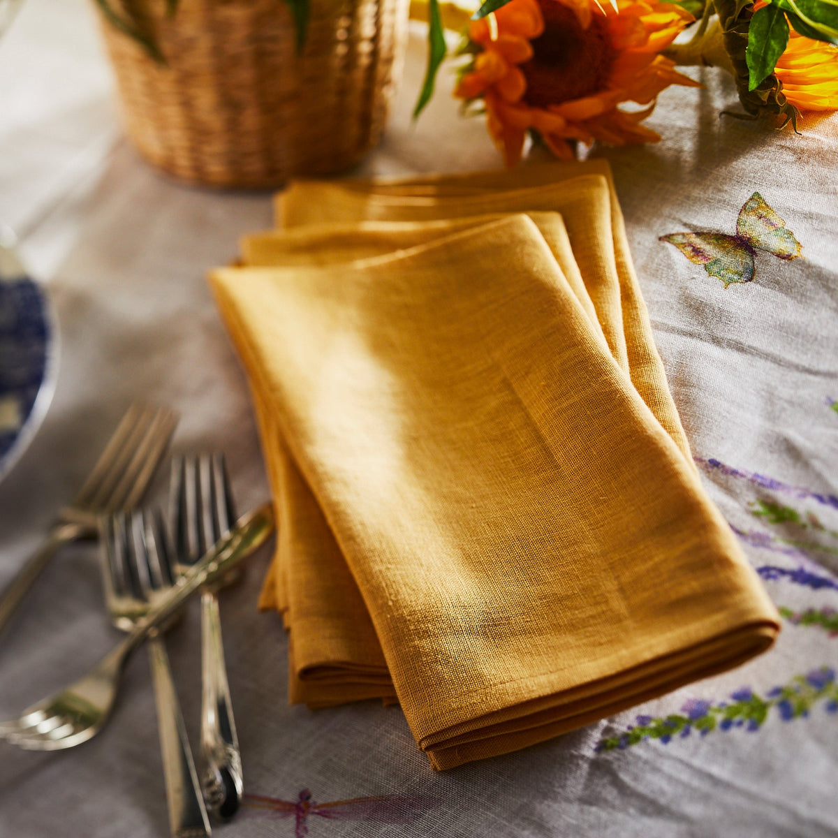 A Marigold Linen Dinner Napkins Set/4 on a table next to a fork and knife. [Brand Name: TTT]