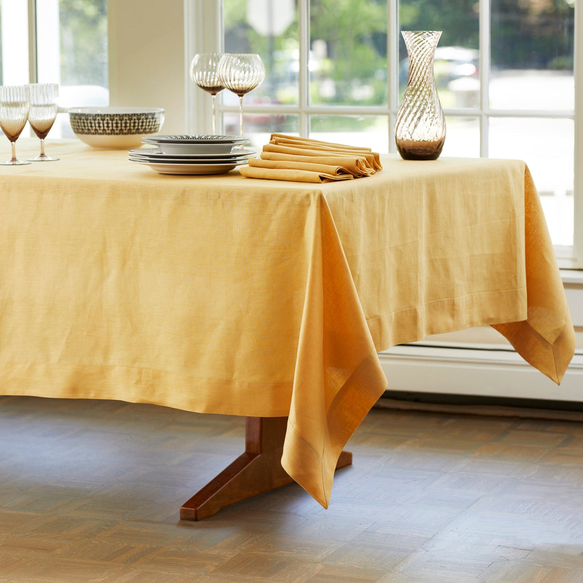 A Marigold Linen Tablecloth and Napkin Set made sustainably from linen sourced from an Italian mill, draped gracefully on a wooden table.