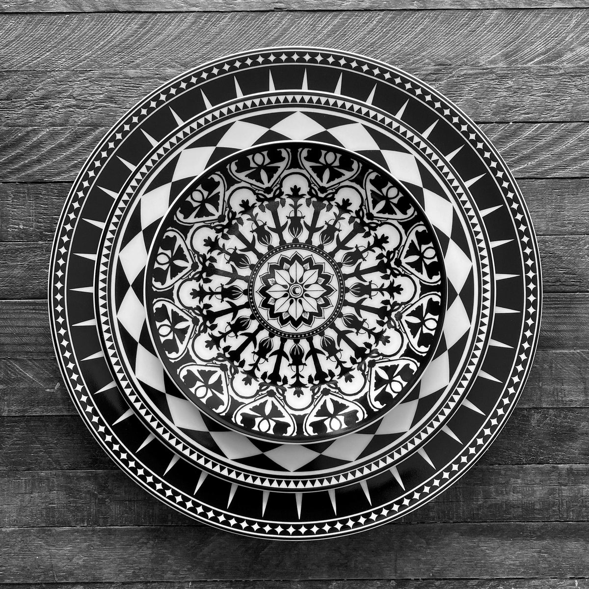 An artistic Marrakech Black Rimmed Dinner Plate captures an exquisite display of Art Deco forms on a simple wooden table by Caskata Artisanal Home.