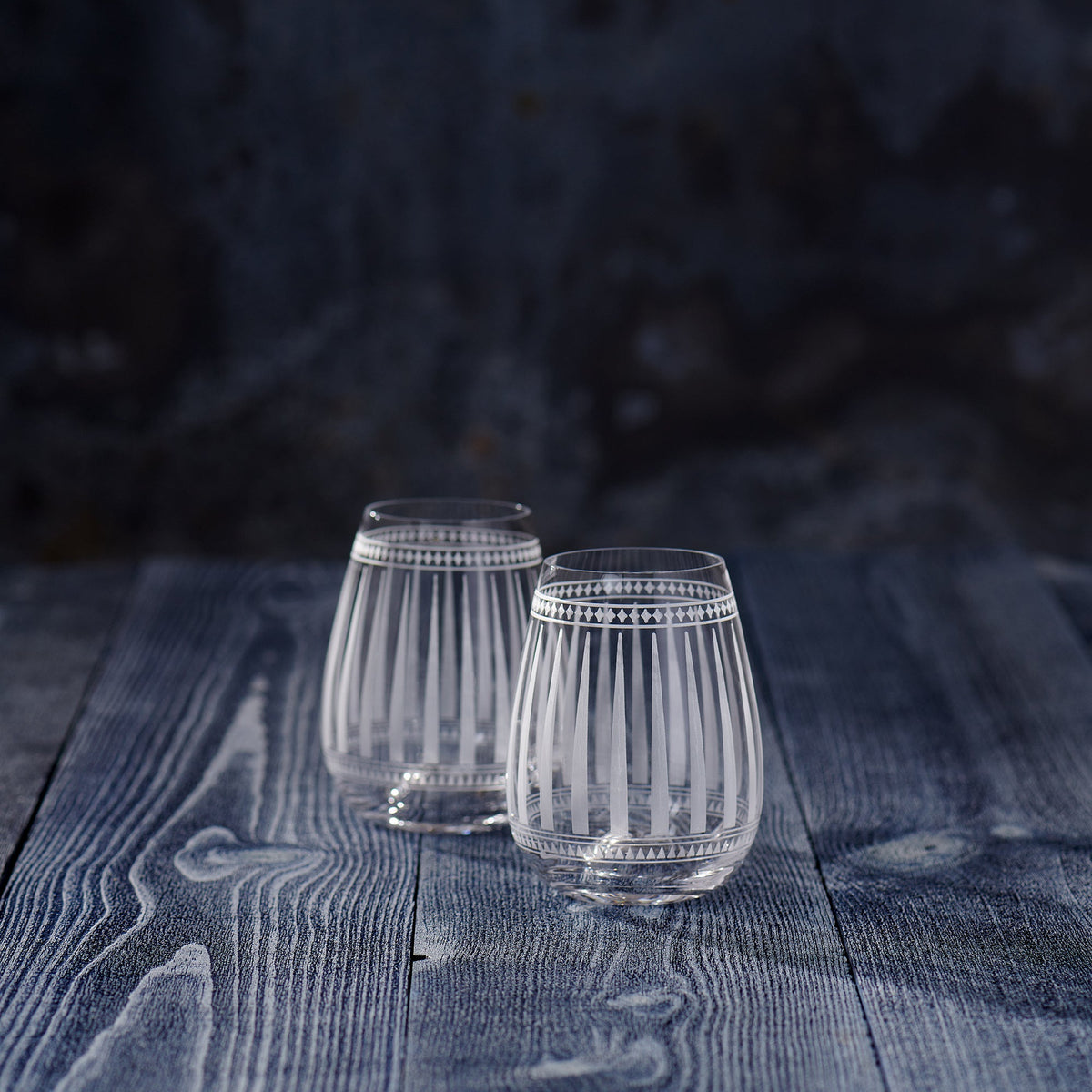 Two Marrakech Stemless Wine Glasses with graphic patterns sitting on top of a wooden table. (Brand: Caskata Artisanal Home)