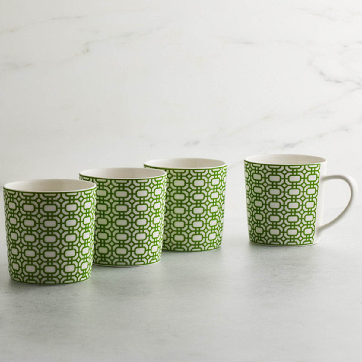 Four Newport Garden Gate Verde Mugs by Caskata Artisanal Home are aligned in a row on a light gray surface with a white marble background.