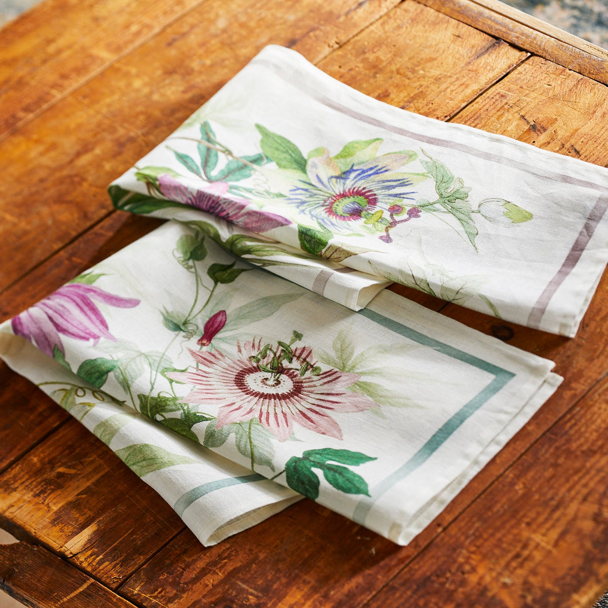 Two Passionflower Linen Kitchen Towels Set/2 with passionflowers on them on a wooden table. (Brand Name: TTT)