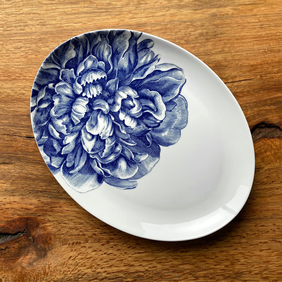 A Peony Medium Coupe Oval Platter with a blue floral pattern, placed on a wooden surface. - Caskata Artisanal Home