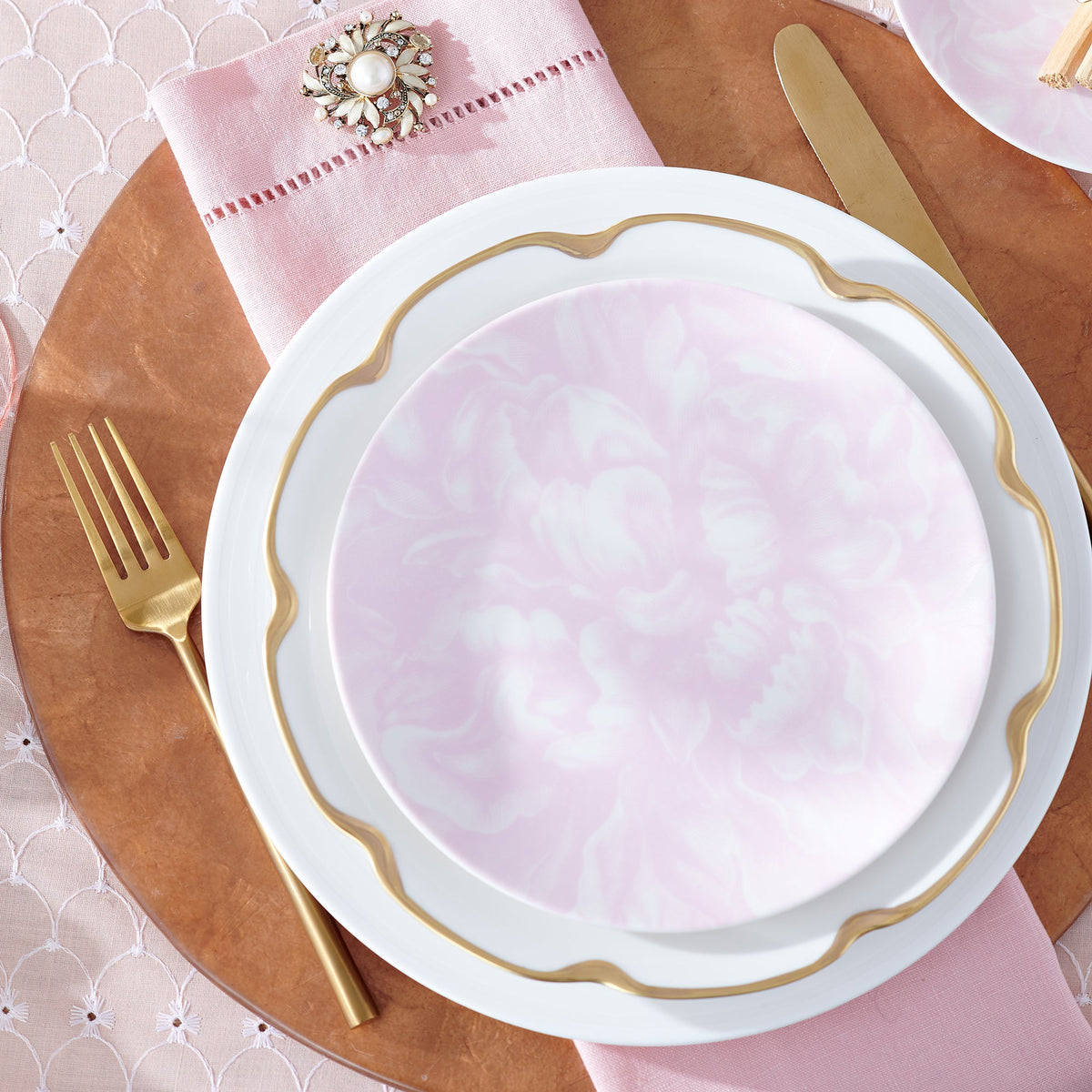 A crisp pink table setting with Caskata Artisanal Home&#39;s Cambridge Stripe White Rimmed Dinner Plate and patterned gold forks and spoons.