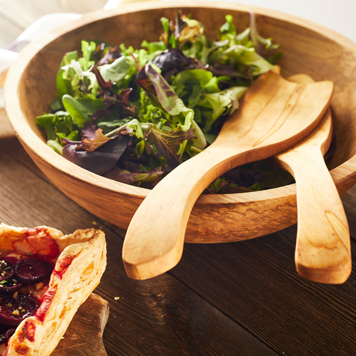 An artisan woodworker&#39;s Peterman&#39;s handmade serving utensils showcase a Spalted Maple wood bowl filled with a fresh salad.