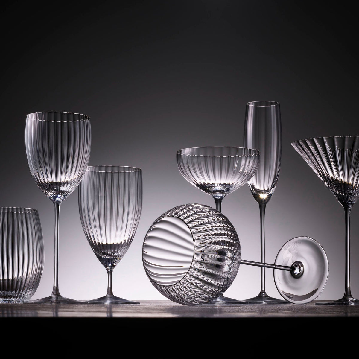 A group of Caskata Artisanal Home Quinn Clear Everyday Glasses on a table in front of a dark background.