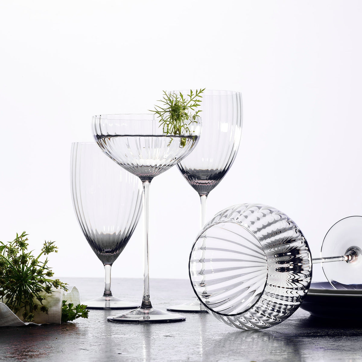 A set of Quinn Clear Everyday Glasses with flowers and greenery on a Caskata Artisanal Home table in Czech Republic.