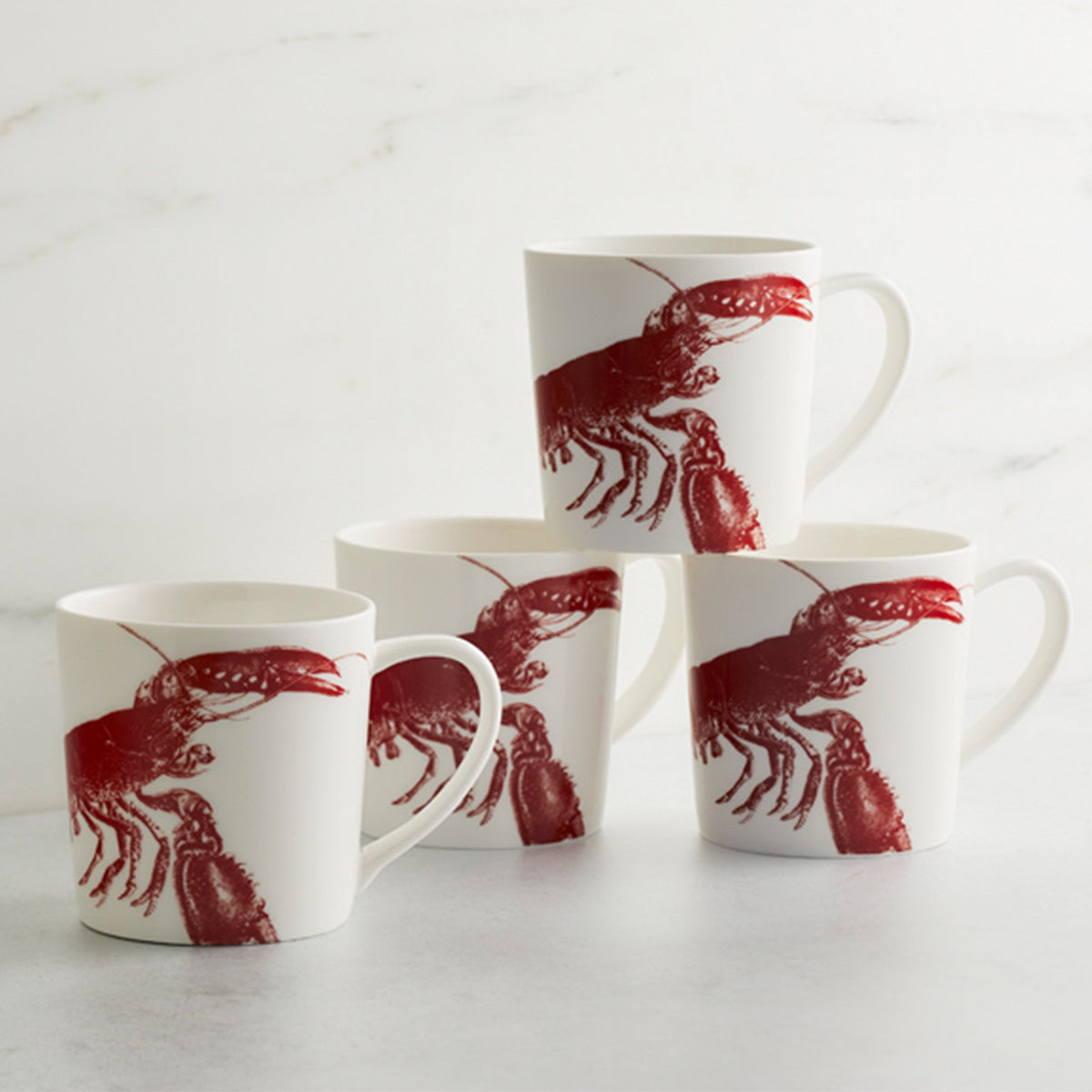 Four white, high-fired Lobster Red Mugs by Caskata Artisanal Home with red illustrations are arranged on a grey surface against a white background, with two mugs stacked on two others, showcasing a charming seaside style.