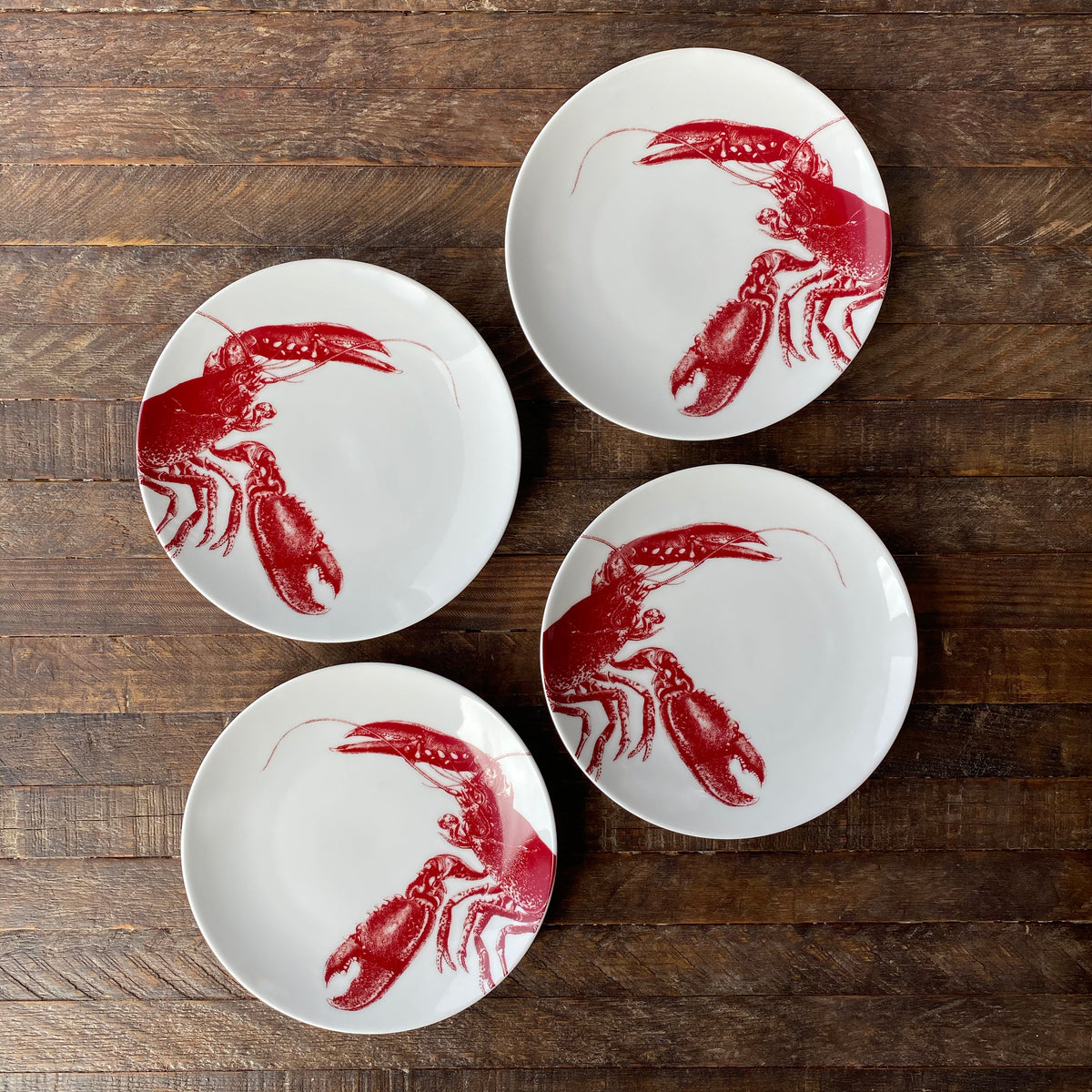 Four **Lobster Red Small Plates** by **Caskata Artisanal Home** arranged on a wooden surface, showcasing heirloom-quality dinnerware with seaside style.