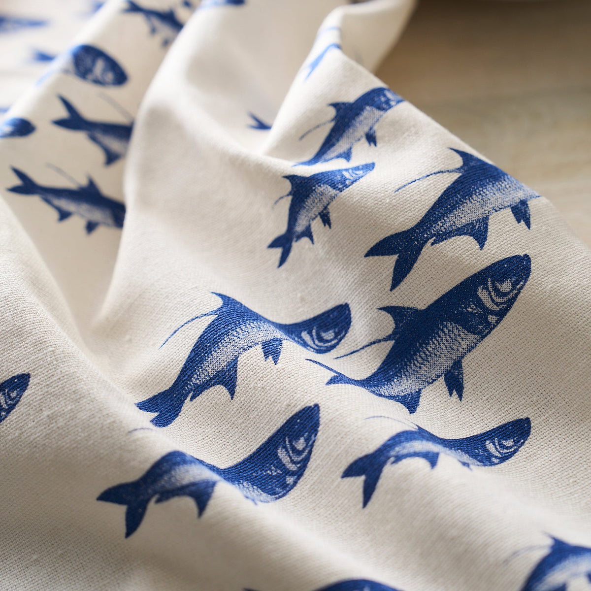 White fabric with a blue fish pattern, from the Caskata School of Fish Kitchen Towels, Set of 2 collection, draped elegantly over a surface.